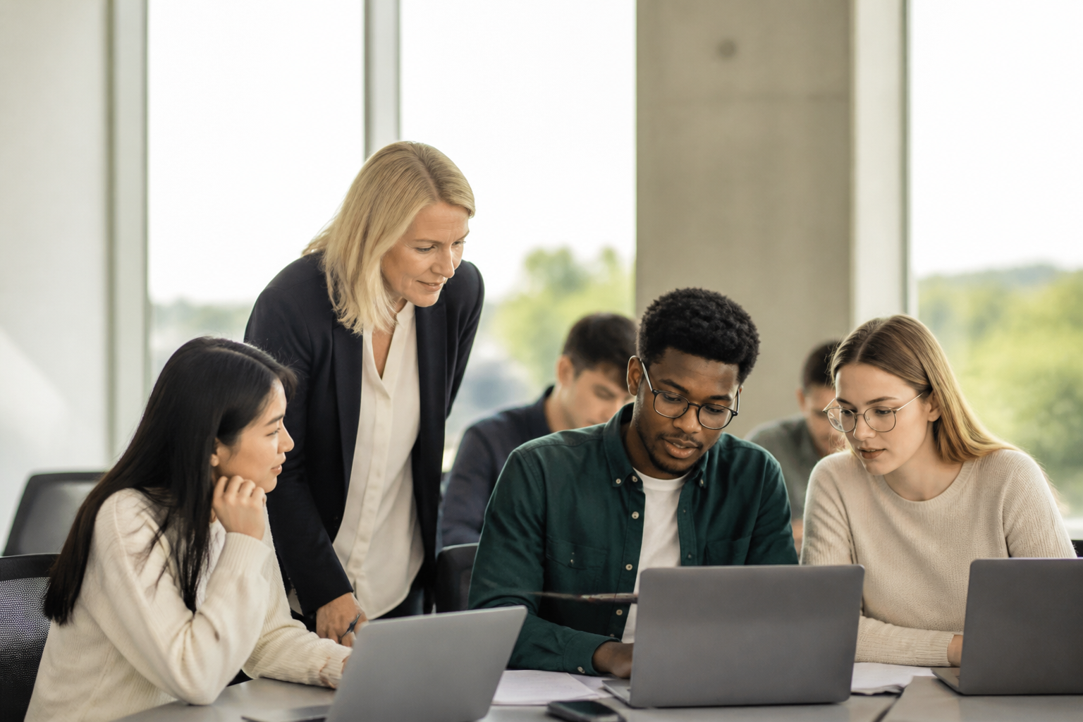 Diverse students collaborating around laptops with an instructor in a seminar room